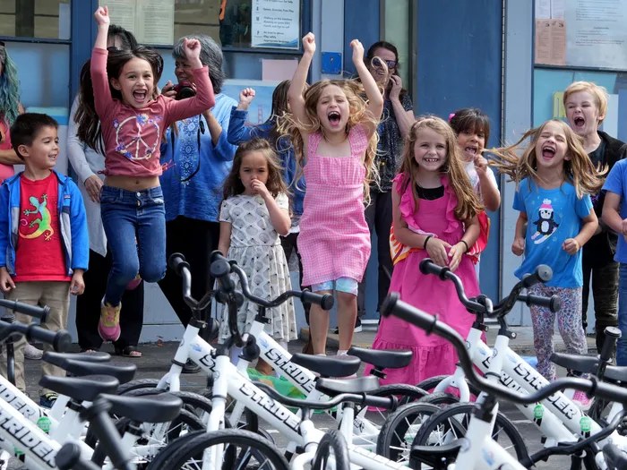Kids cheer behind a row of new balance bikes at a youth bike giveaway